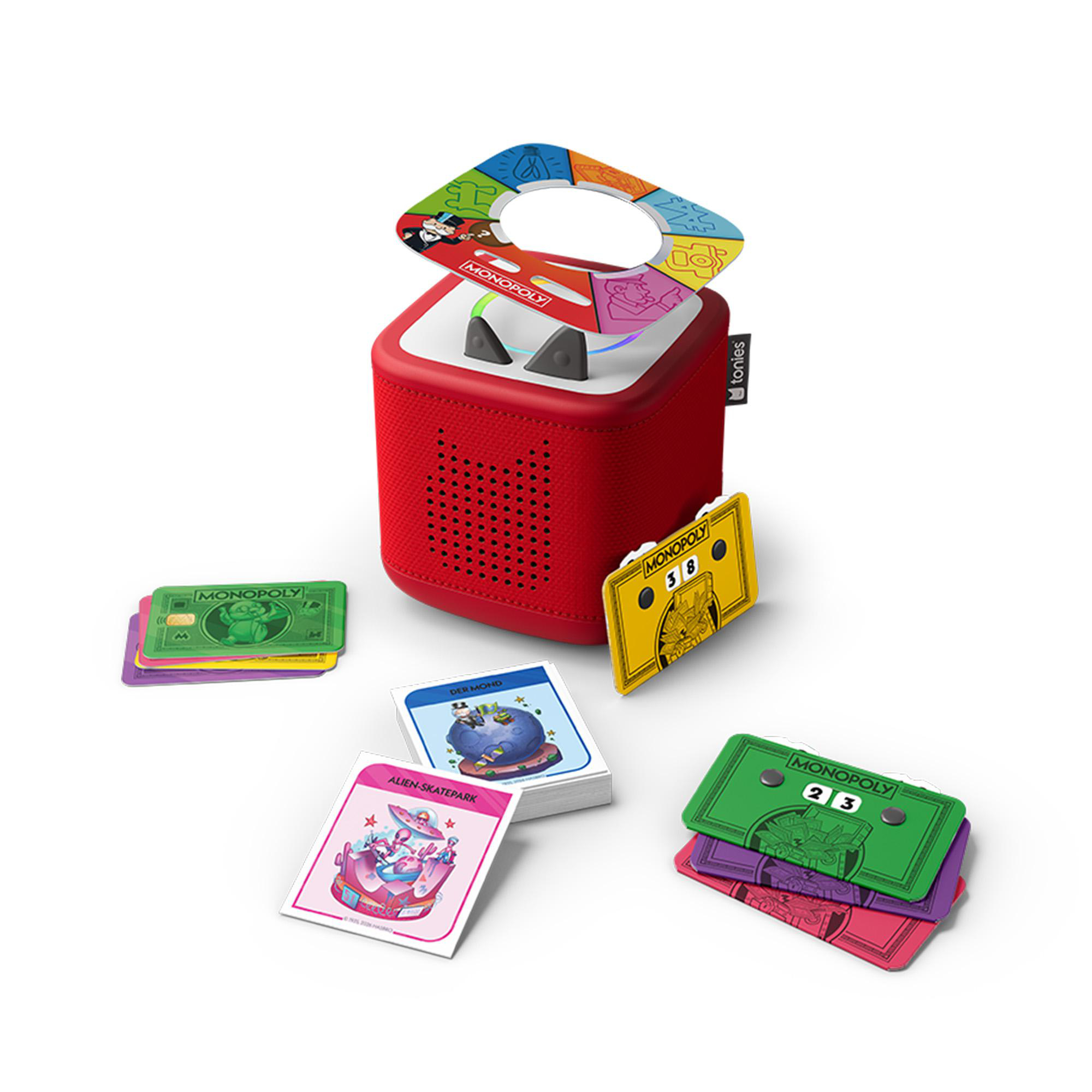Ein roter Toniebox-Lautsprecher mit Monopoly-Zubehör, einschließlich Figuren, Karten und farbigen Aufsätzen auf weißem Hintergrund.