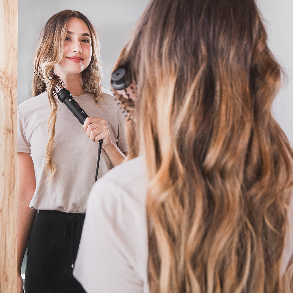 Una mujer con una camiseta clara se mira en el espejo y se peina el cabello.