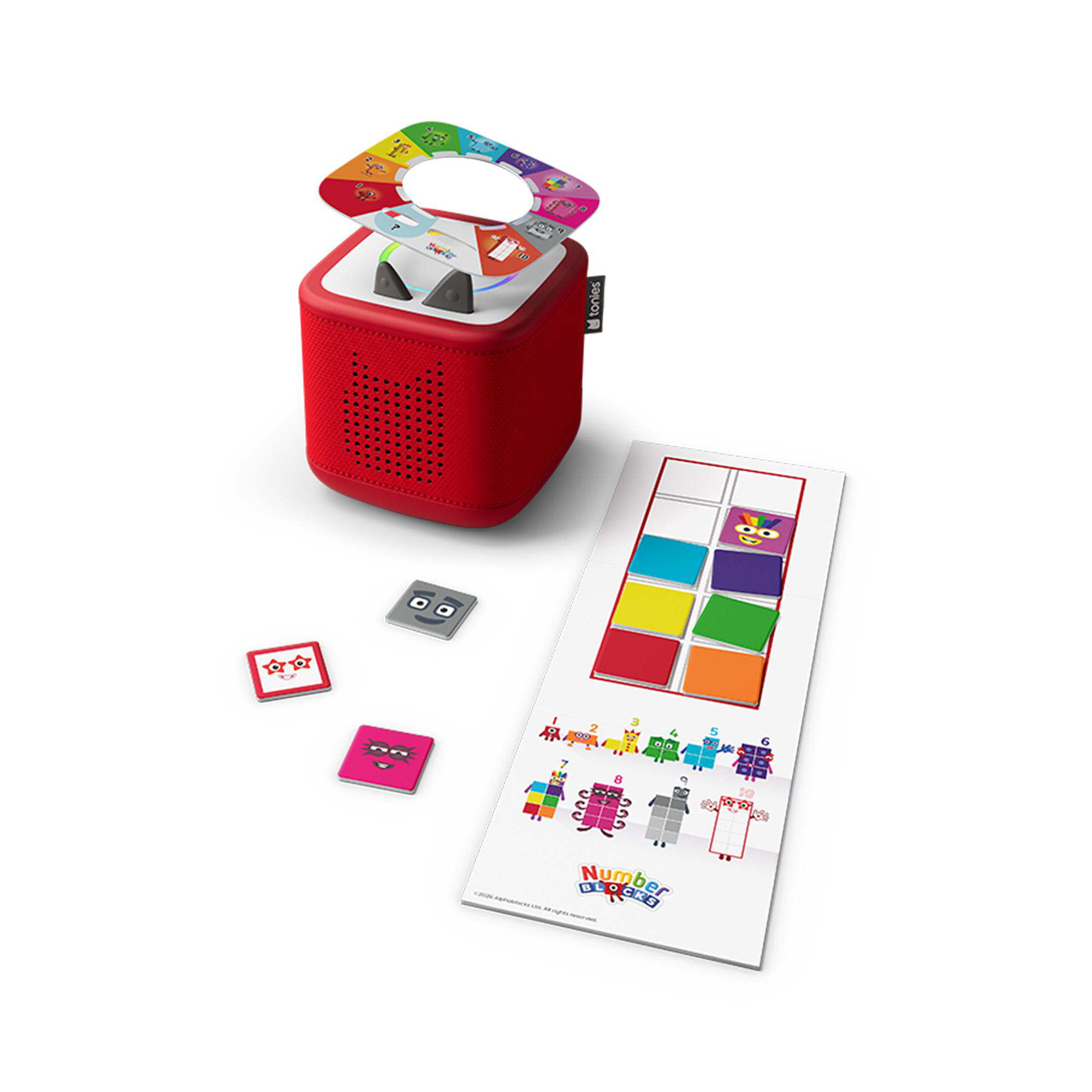 Eine rote Toniebox mit bunter Magnetring-Verzierung, kleinen quadratischen Figuren und einer Numberblocks-Spielunterlage.