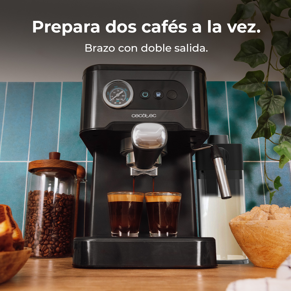 Una cafetera negra prepara dos tazas de café a la vez, con un tarro de granos y un recipiente de leche al lado.