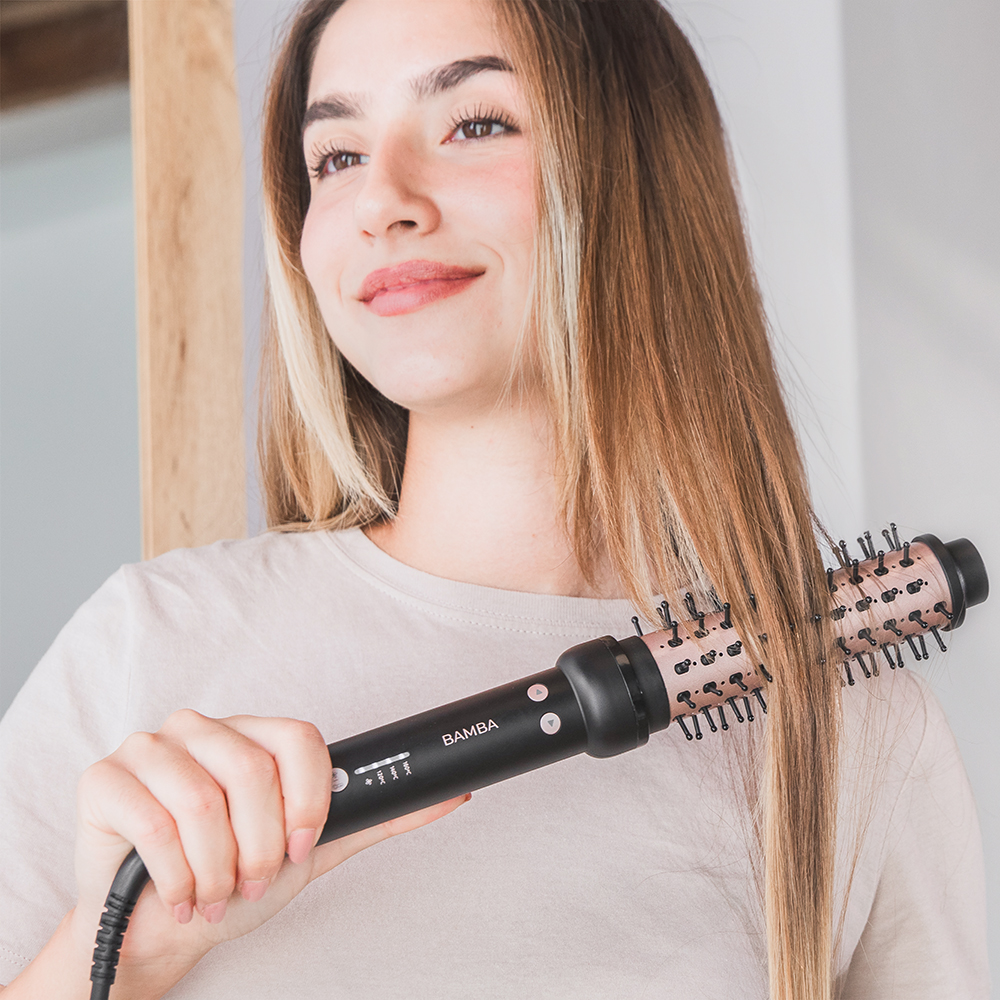 Una mujer sonriente se peina su largo cabello liso con un cepillo de aire Bamba.