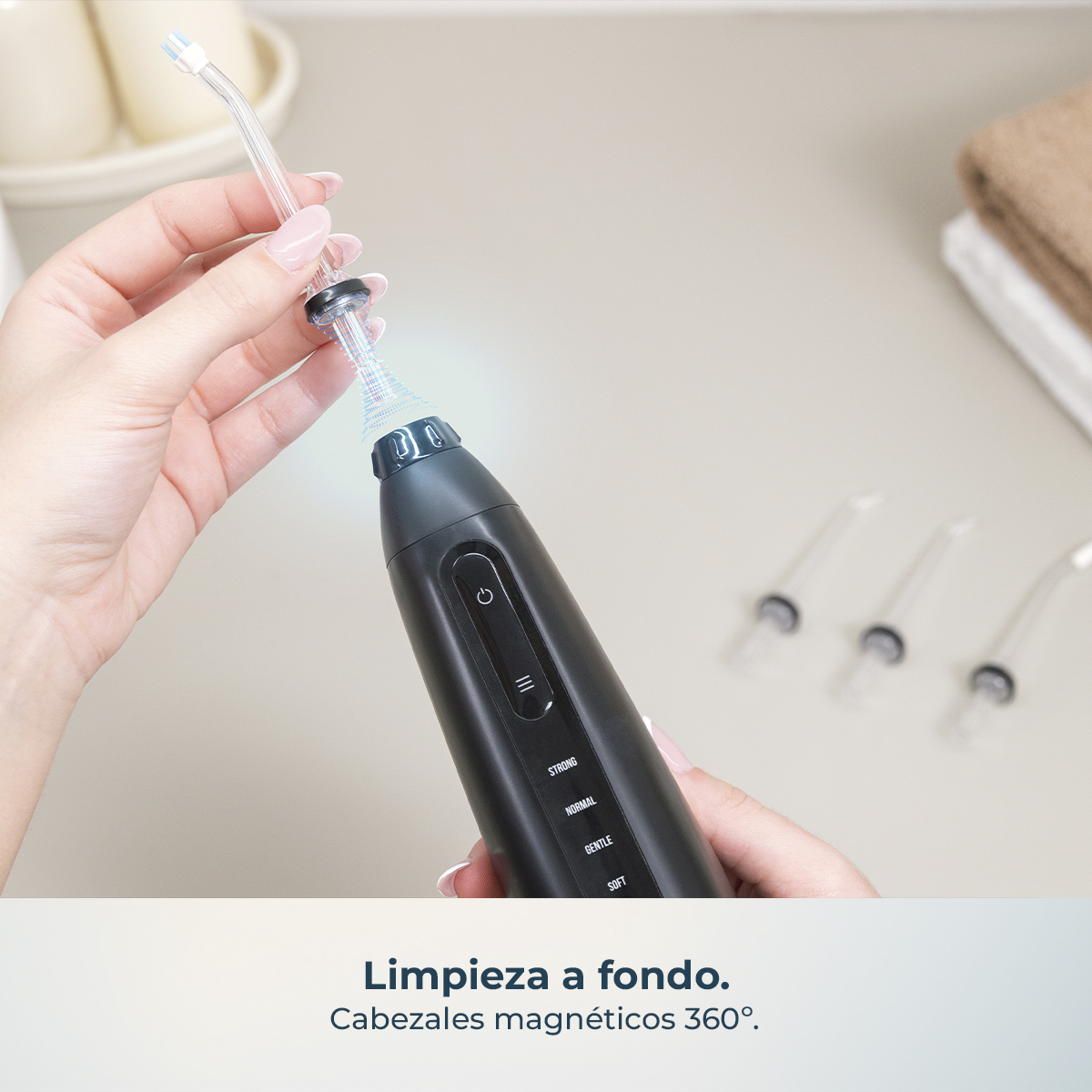 Una mano coloca una boquilla en un irrigador dental negro, con más boquillas y toallas de fondo.