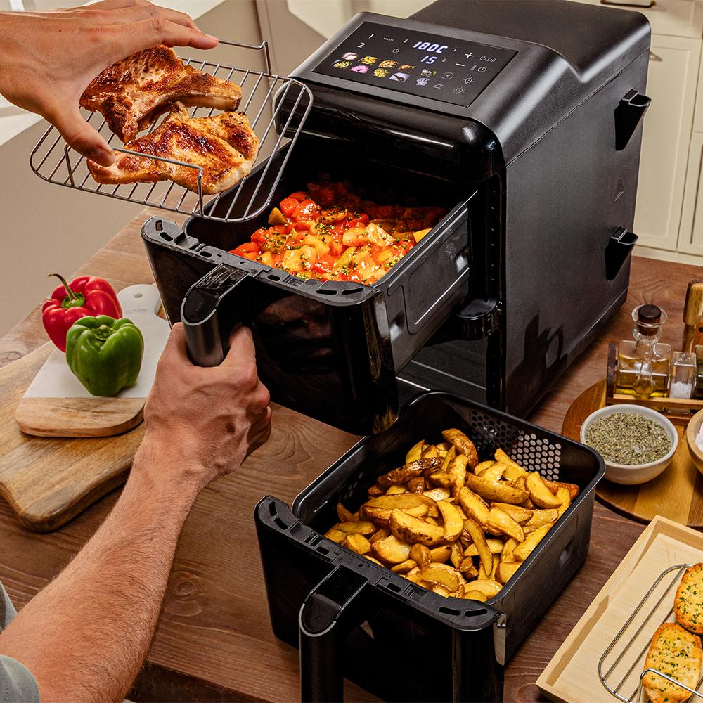 Una persona usa una freidora de aire de doble cesta para cocinar carne, verduras y patatas.