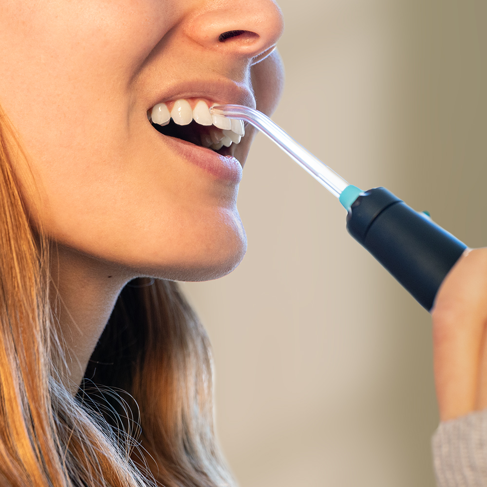 Una mujer usando un irrigador bucal en sus dientes.