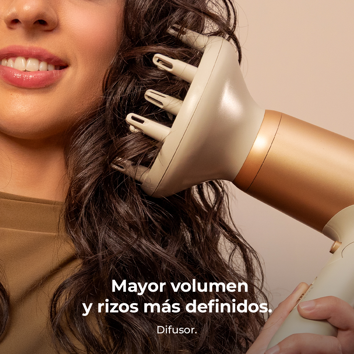 Una mujer seca su cabello rizado con un secador difusor dorado. Texto: Mayor volumen.
