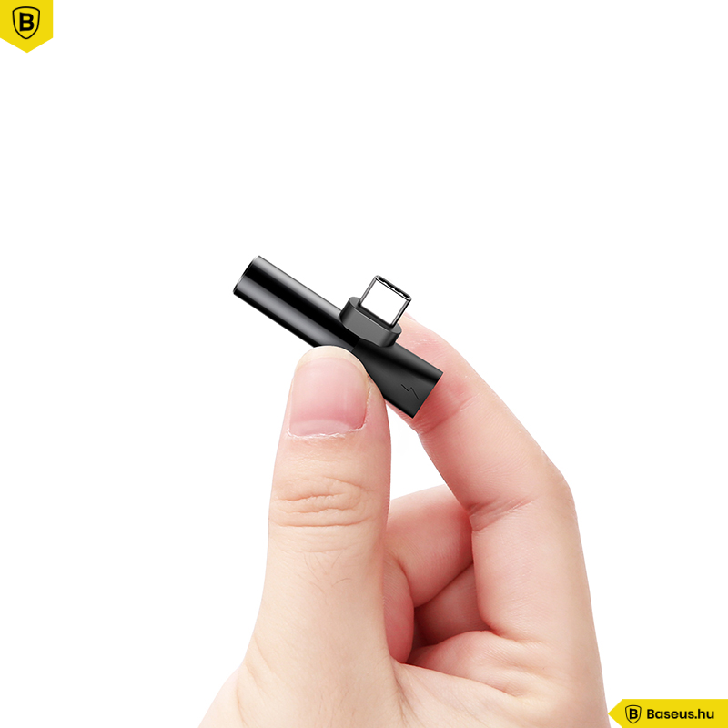 Egy kéz egy kis fekete USB-C adaptert tart fehér háttér előtt.