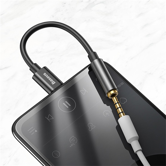 Egy fekete audiókábel adapterrel csatlakozik egy okostelefonhoz fehér márványon.