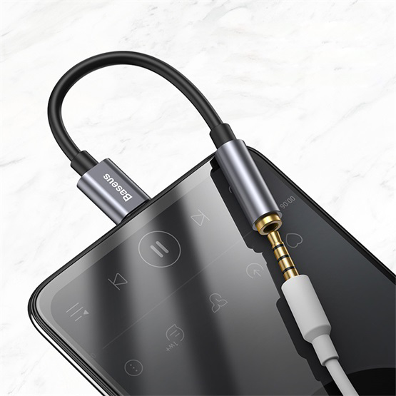 Fekete audio adapterkábel okostelefonba dugva, világos márványos felületen.