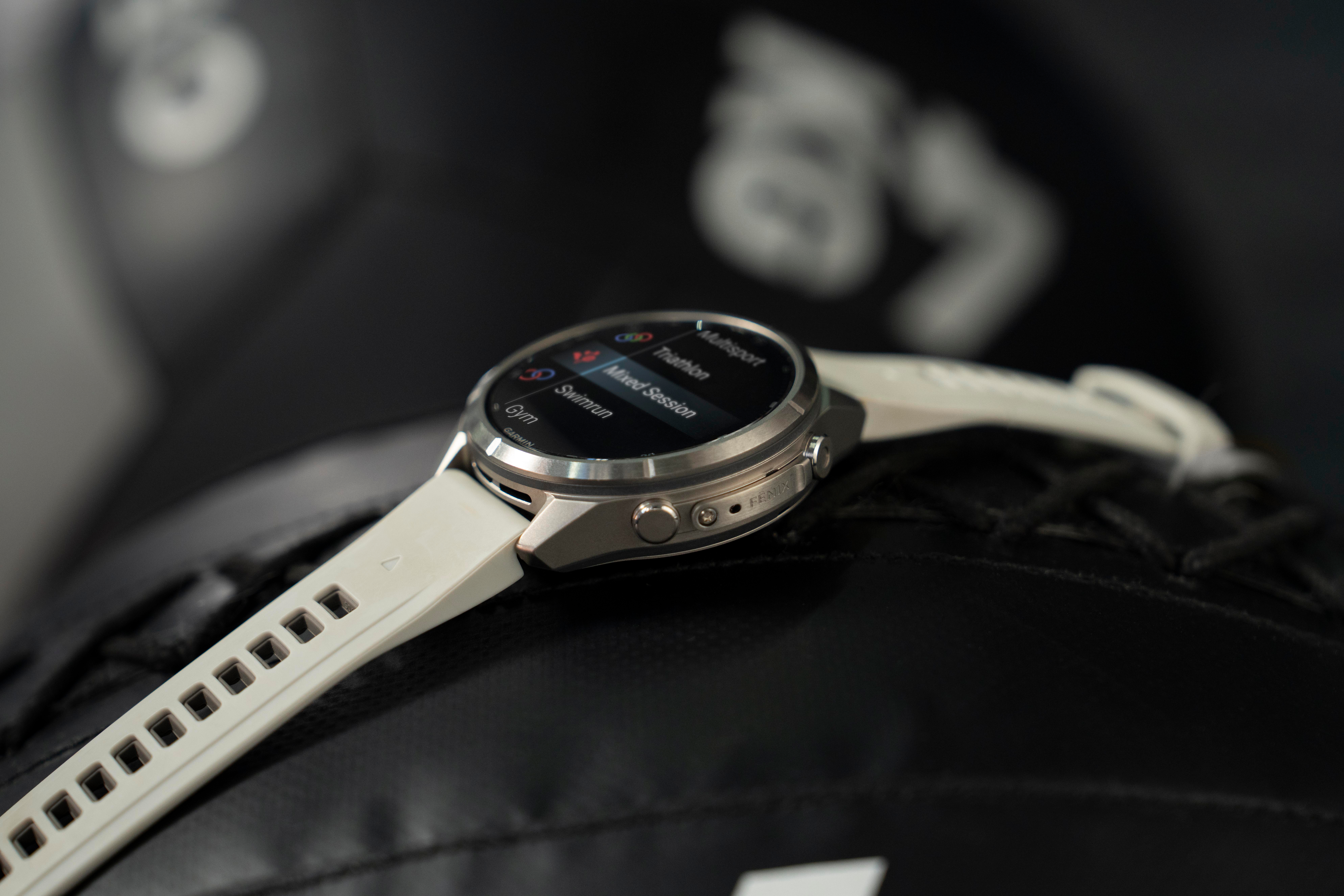 Eine silberne Garmin-Sportuhr mit weißem Armband liegt auf einer dunklen Oberfläche mit Trainingsoptionen im Display.
