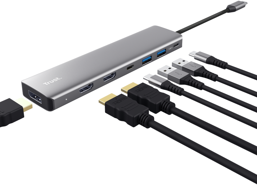 Grauer Trust USB-C-Hub mit angeschlossenen HDMI- und USB-Kabeln vor schwarzem Hintergrund.