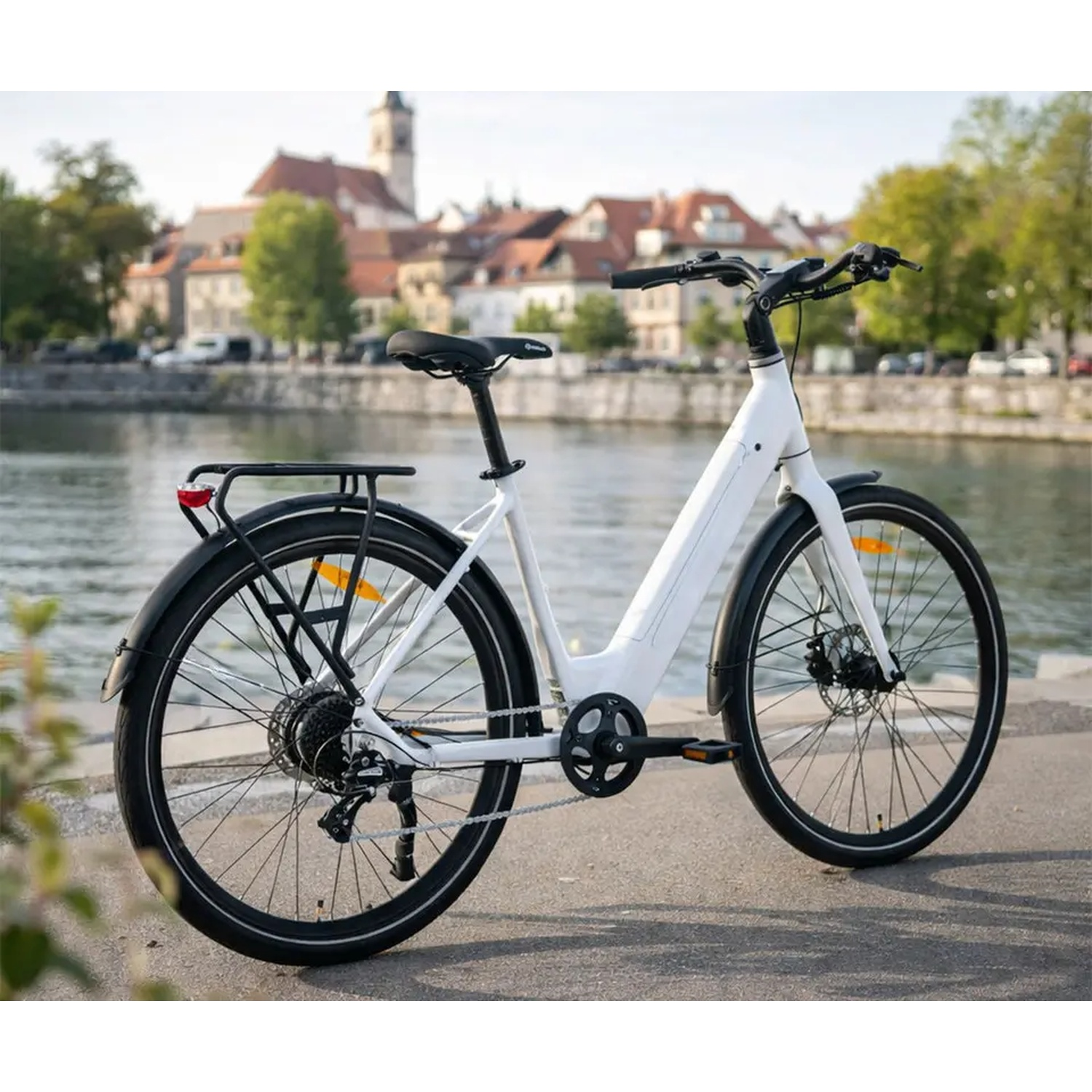 Un vélo électrique blanc garé au bord d'une rivière, avec un paysage urbain et des bâtiments en arrière-plan.