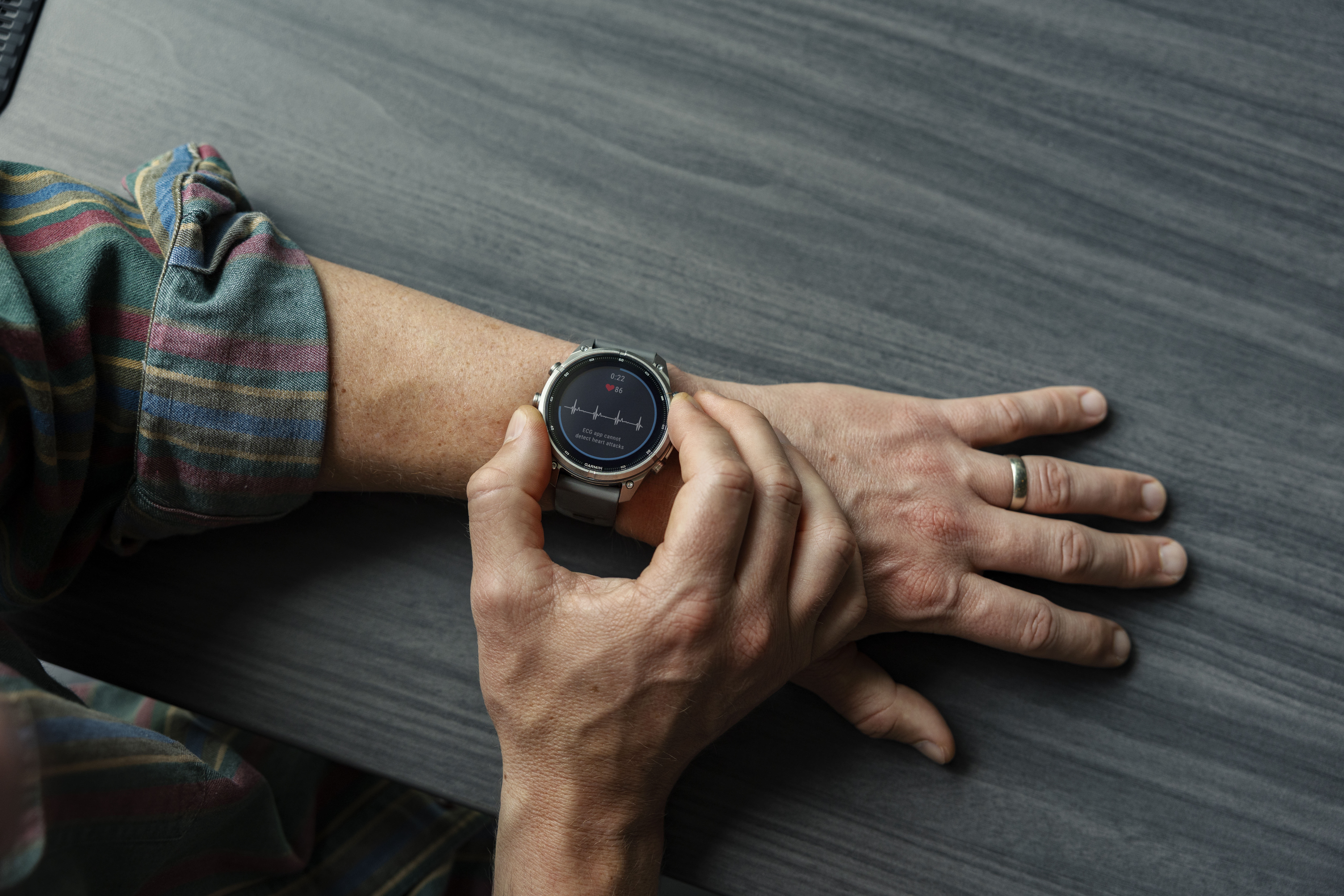 Eine Person drückt die Tasten einer Smartwatch am Handgelenk auf einem Holztisch.