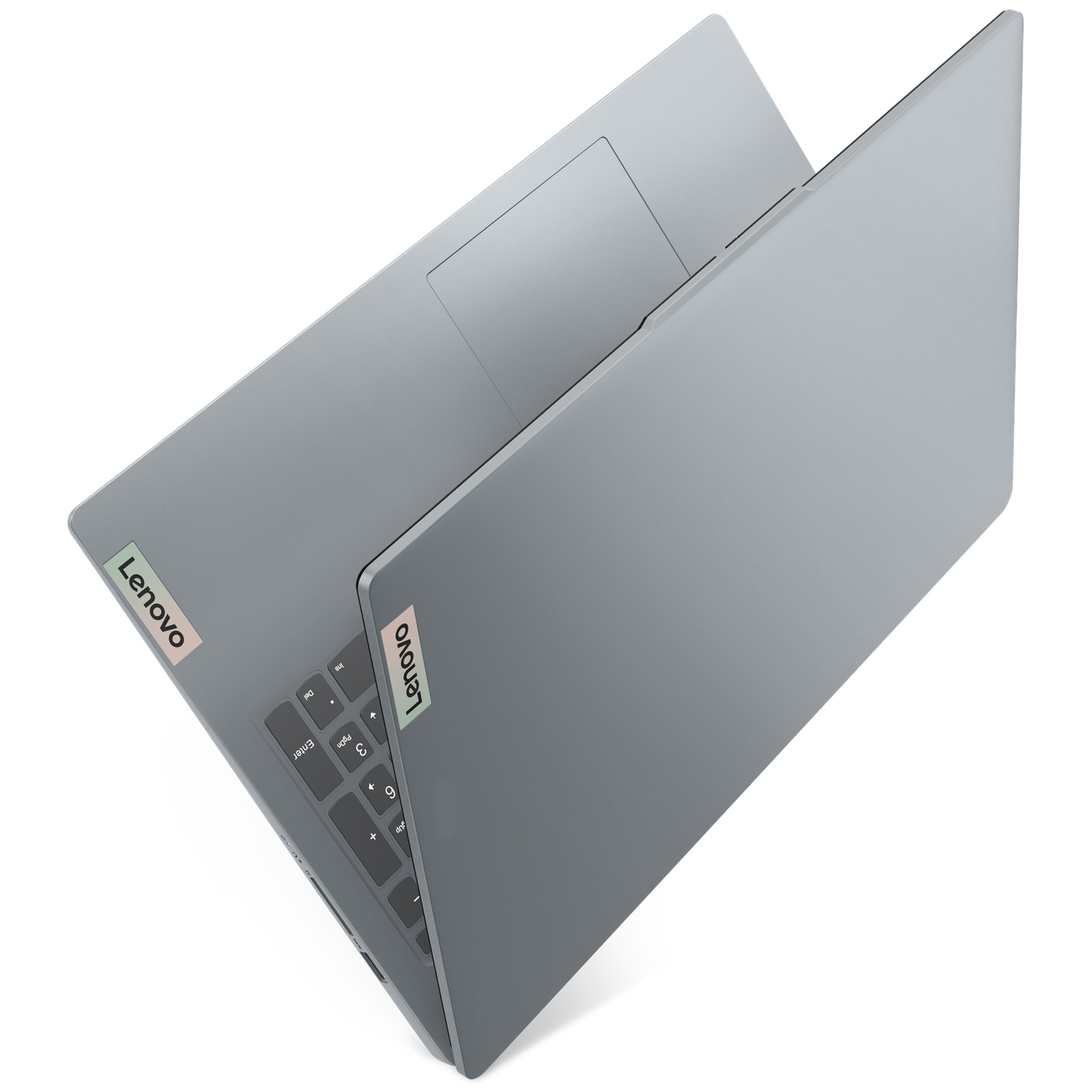 Un ordinateur portable Lenovo gris est partiellement ouvert sur une surface blanche, montrant son logo et son clavier.