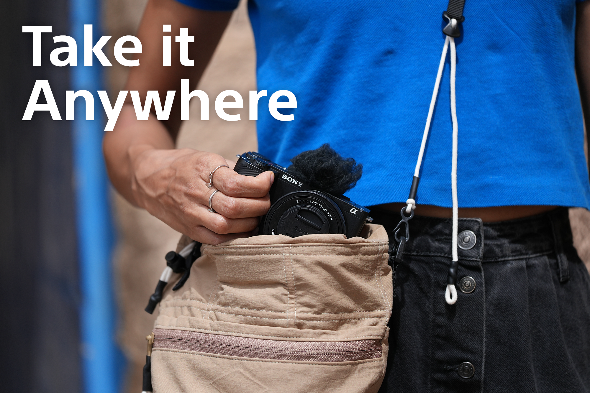 Person in blauem Hemd holt Sony-Kamera aus einer beigen Umhängetasche; Text "Take it Anywhere".