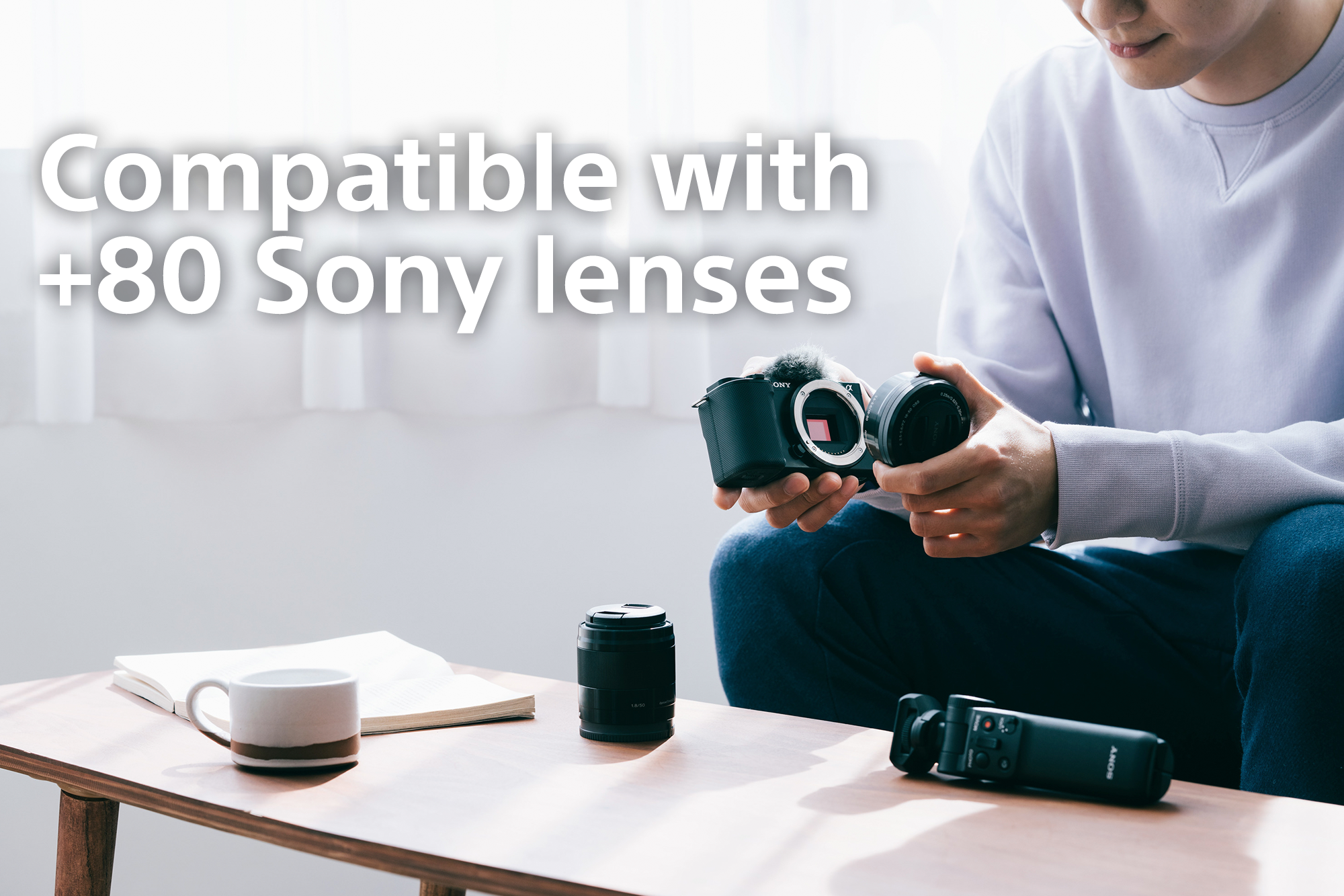Eine Person hält eine Kamera und ein Objektiv in einem Raum, mit Text Kompatibel mit +80 Sony-Objektiven.