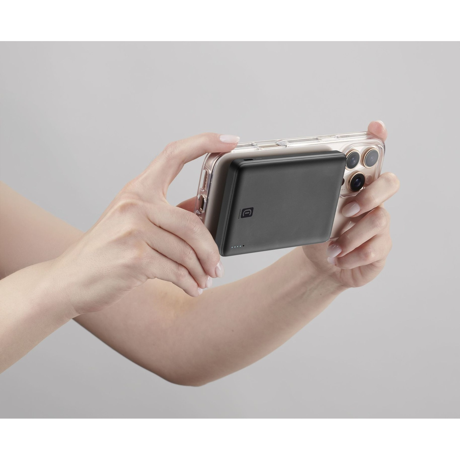 Mani che reggono uno smartphone con un power bank nero sul retro su sfondo grigio.