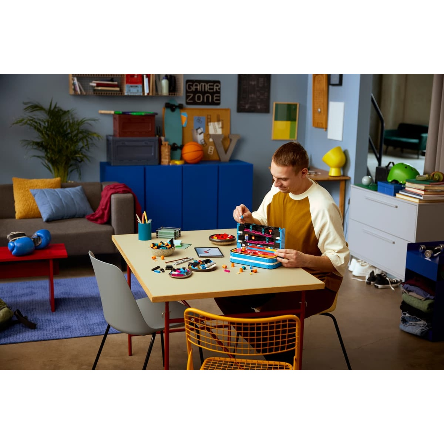 Un uomo siede a un tavolo costruendo un piccolo set Lego in una stanza colorata con divano e mobile blu.