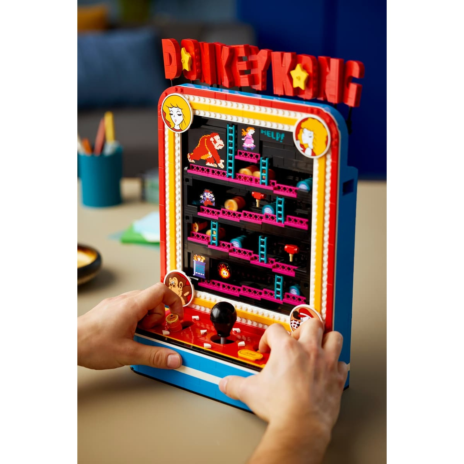 Un colorato cabinetto arcade di Donkey Kong costruito con mattoncini LEGO, con mani che toccano joystick e pulsanti.