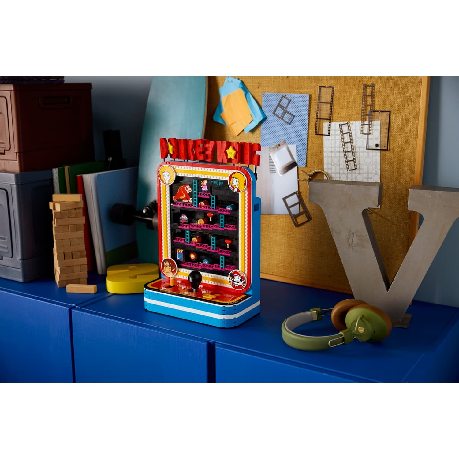 Un cabinato arcade Lego Donkey Kong su un mobile blu, circondato da una bacheca e cuffie.