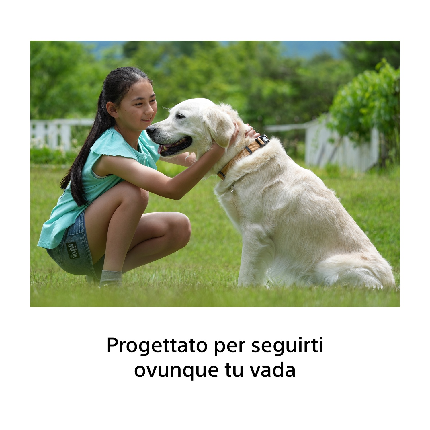 Una bambina accovacciata nell'erba accarezza un grande golden retriever.