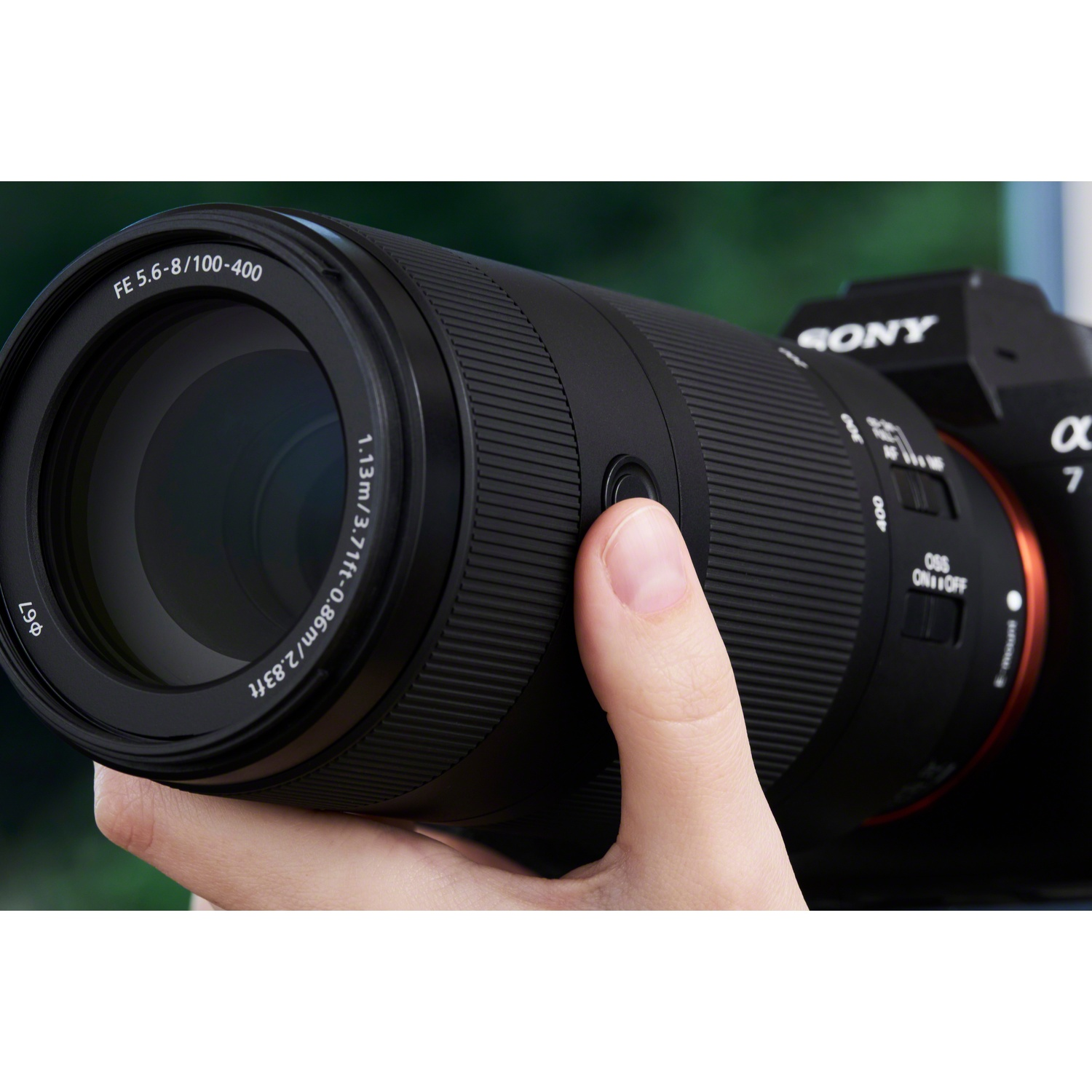 Una mano tiene una fotocamera Sony nera con un grande teleobiettivo su uno sfondo verde sfocato.