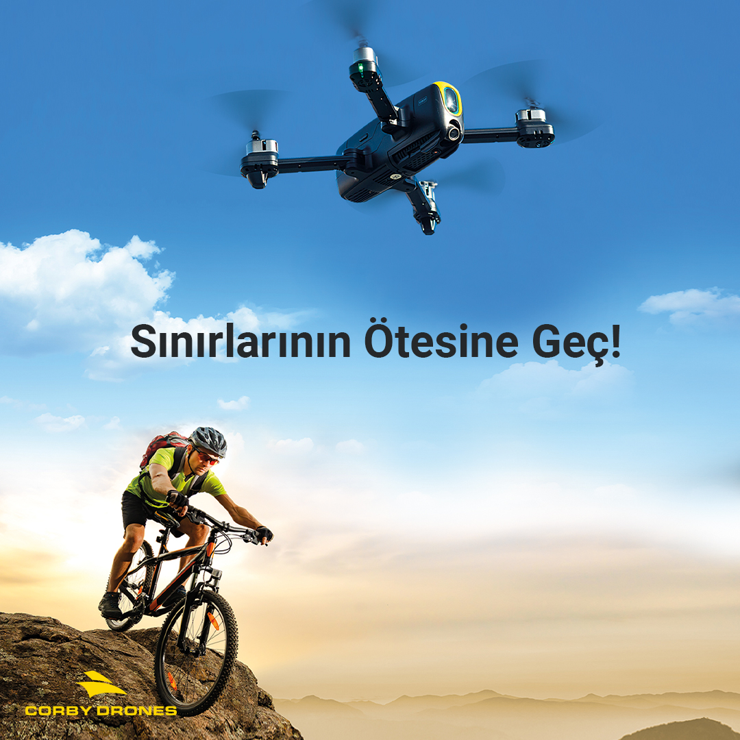 Mavi gökyüzünde bir kayalıkta bisiklet süren dağ bisikletçisinin üstünde uçan bir drone.