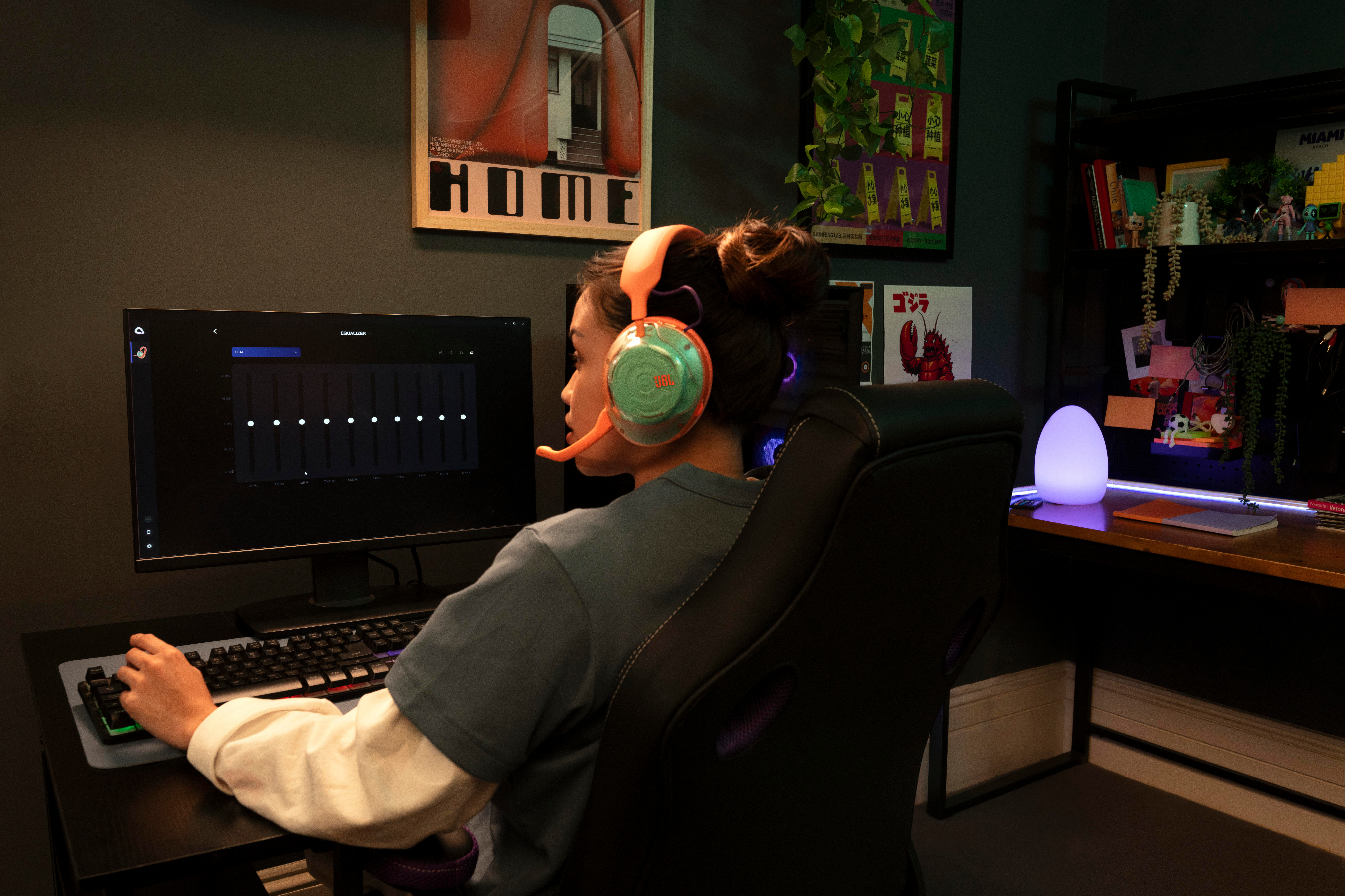 Eine Spielerin sitzt an einem Schreibtisch vor einem Computer, trägt ein buntes Headset und tippt auf eine Tastatur.