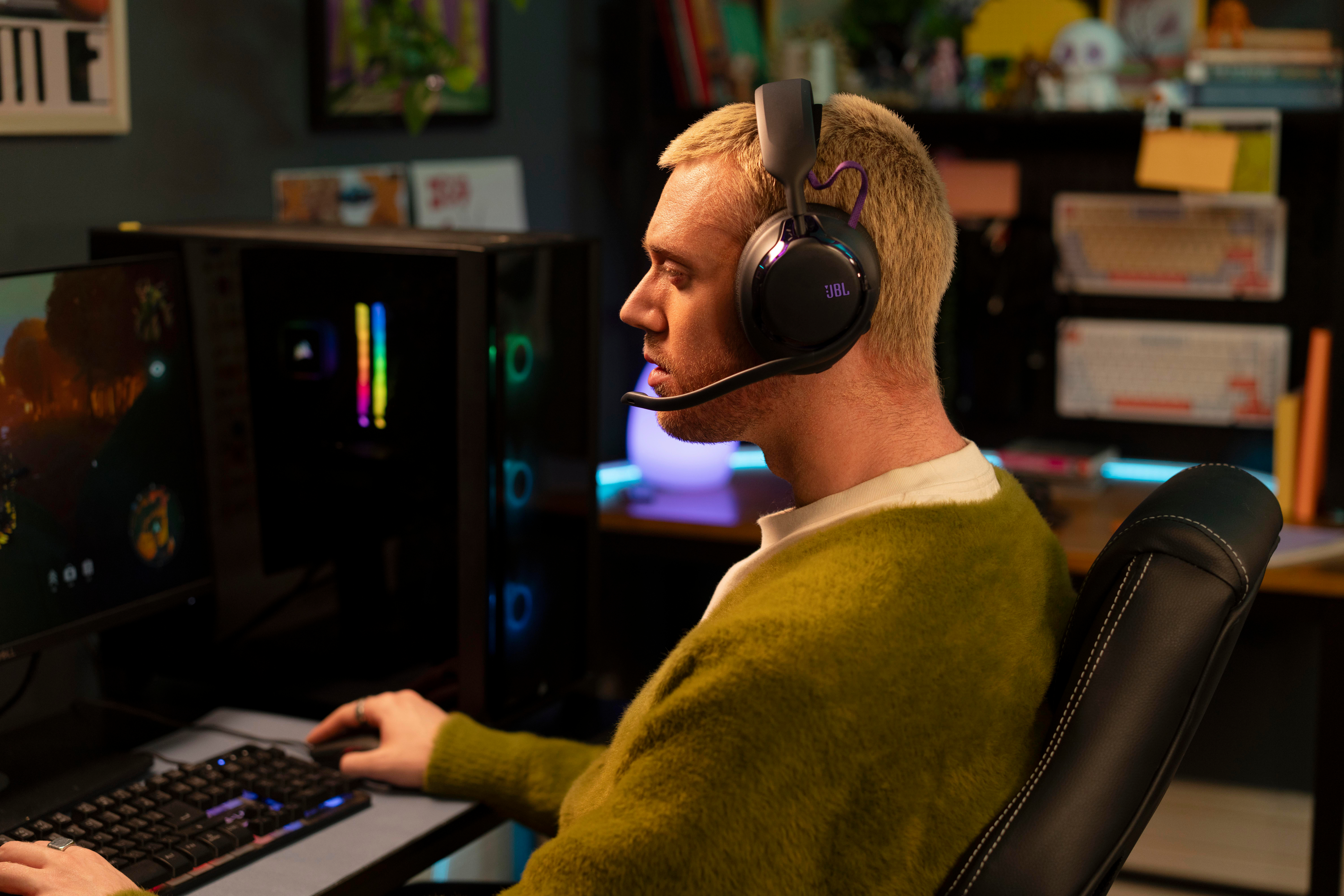 Ein junger Mann mit blonden Haaren sitzt am PC, trägt ein Headset und spielt ein Spiel in einem dunklen Zimmer.