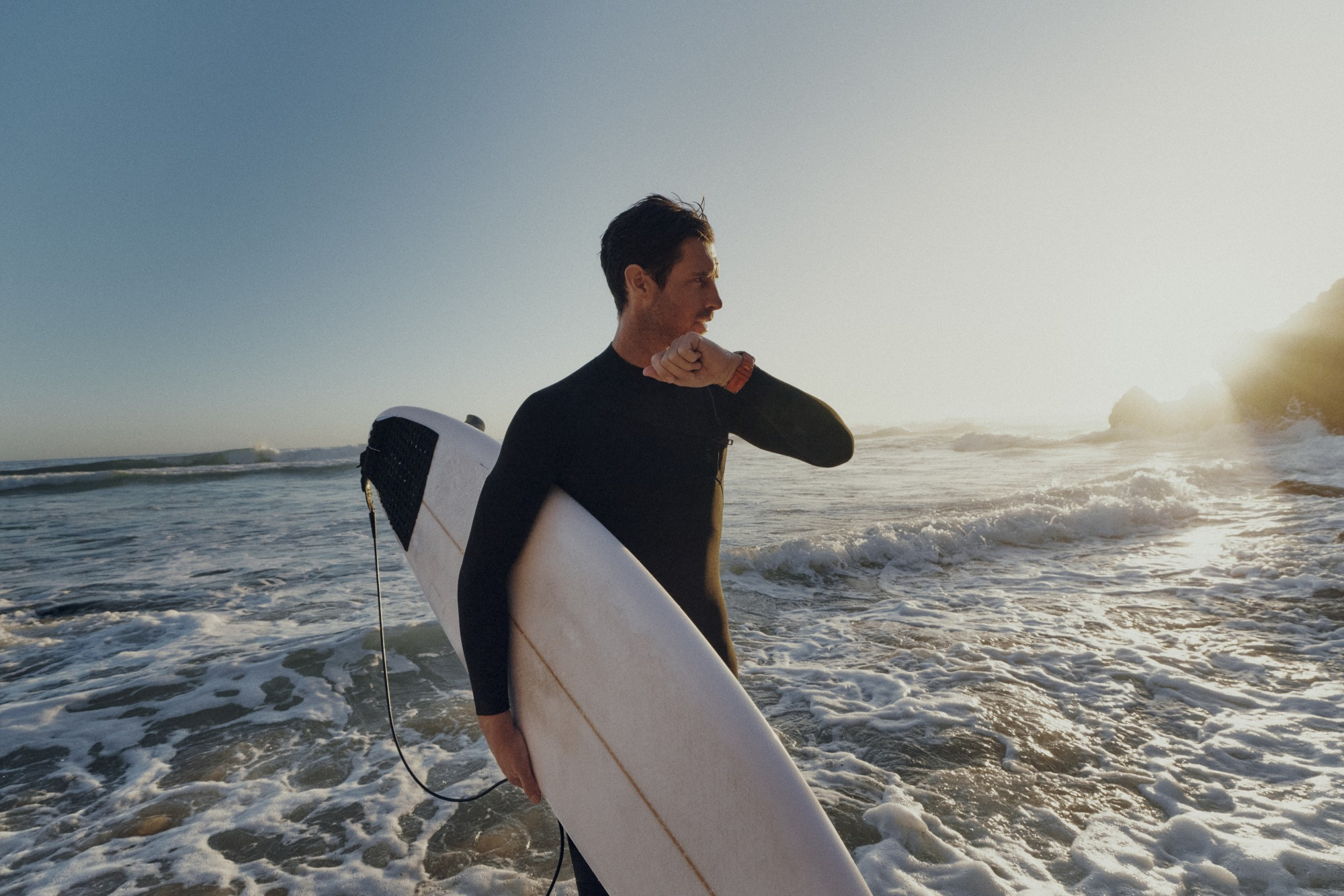 Surfer w piance trzyma deskę na słonecznej plaży z falami.
