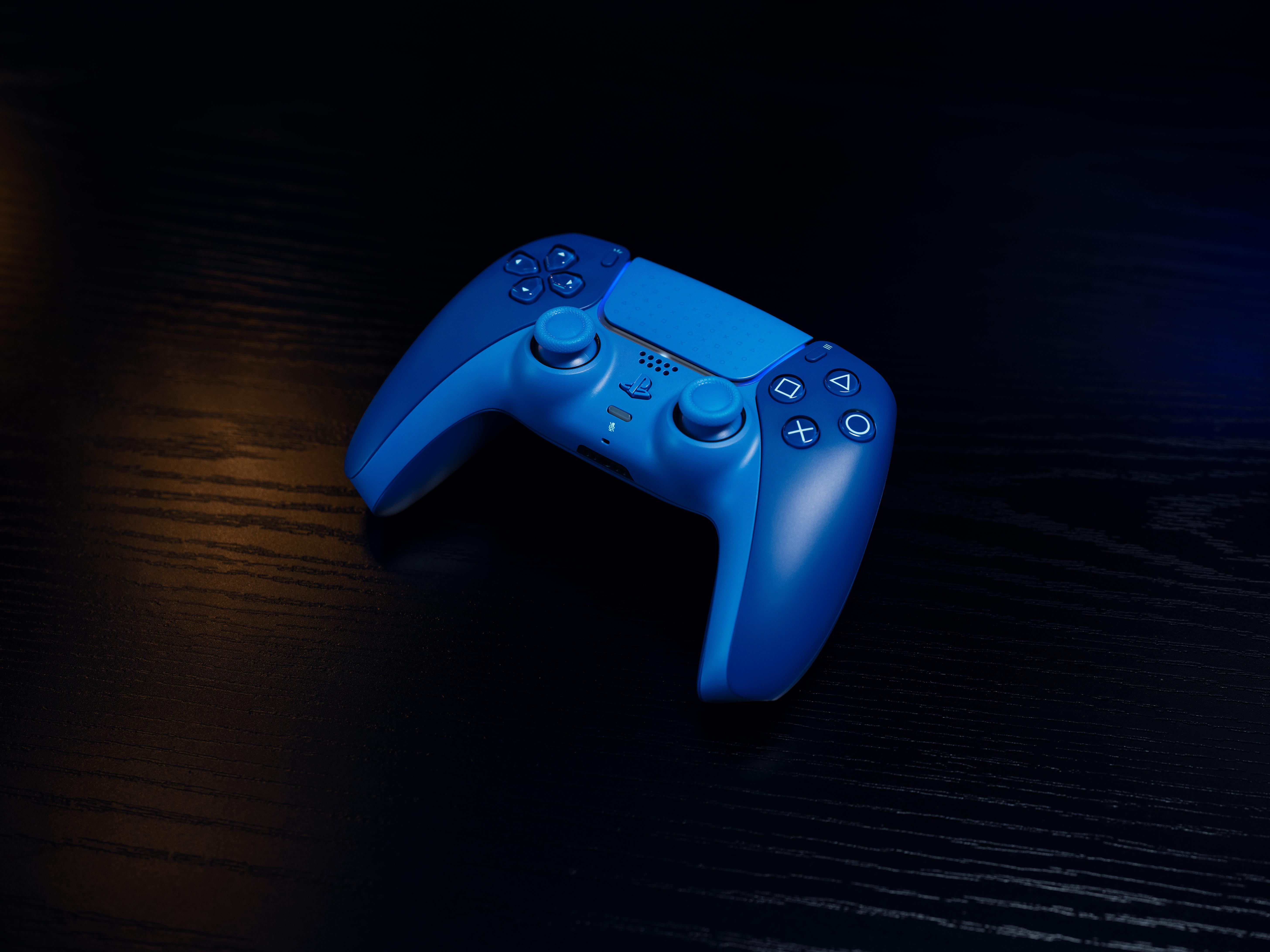 Ein blauer PlayStation 5 Controller auf einem dunklen Holztisch mit stimmungsvoller Beleuchtung.