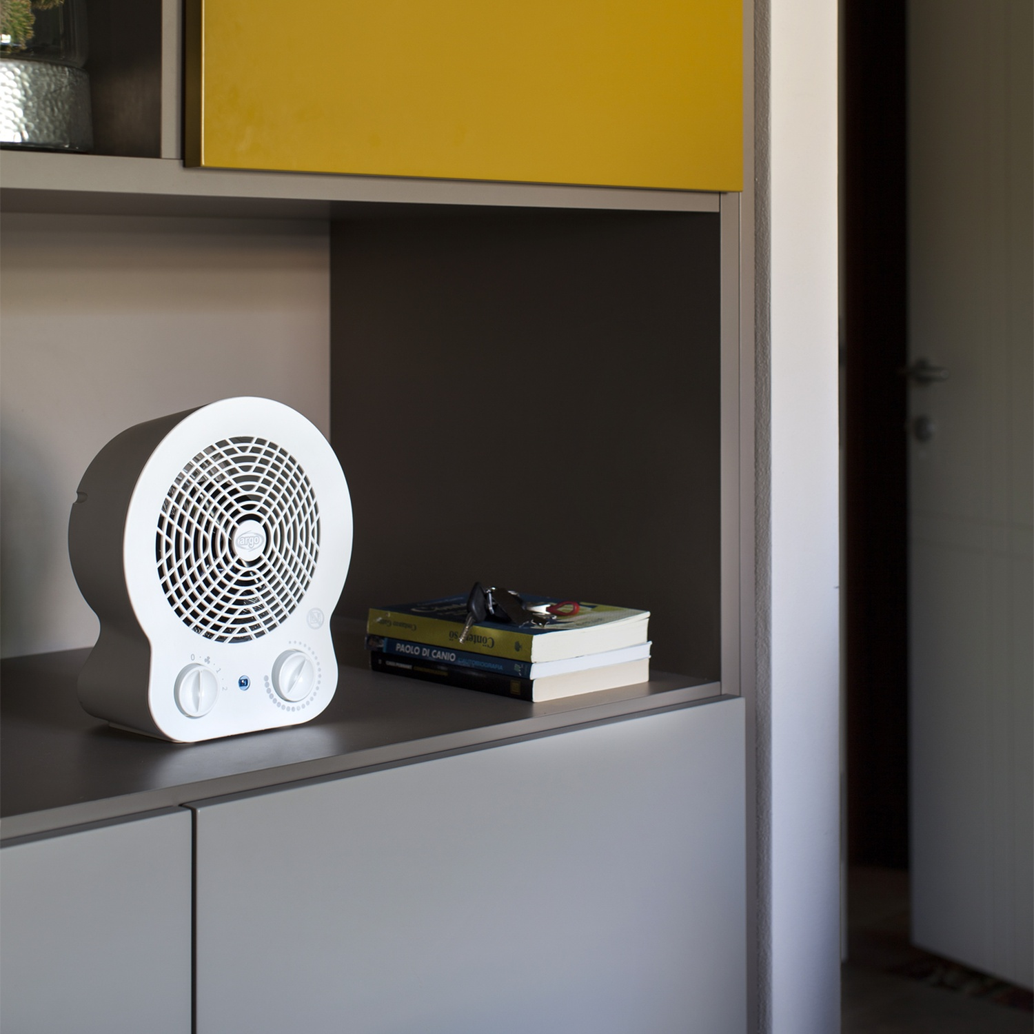 Un termoventilatore bianco è posizionato su un ripiano grigio accanto a dei libri con chiavi.