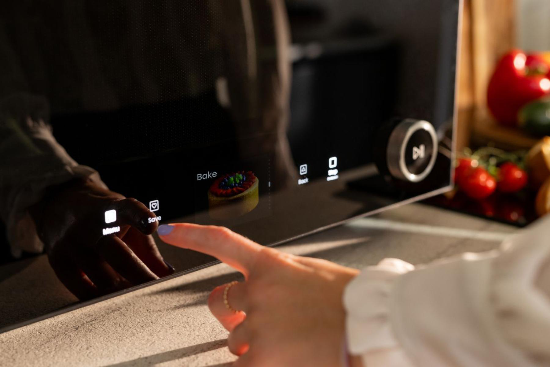 Eine Person tippt auf den Touchscreen eines schwarzen Küchengeräts mit Back-Option.