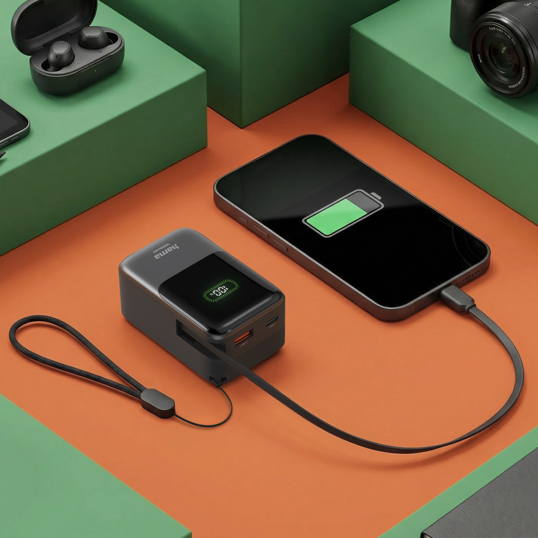 Egy powerbank egy fekete okostelefont tölt narancssárga felületen, zöld blokkokkal.