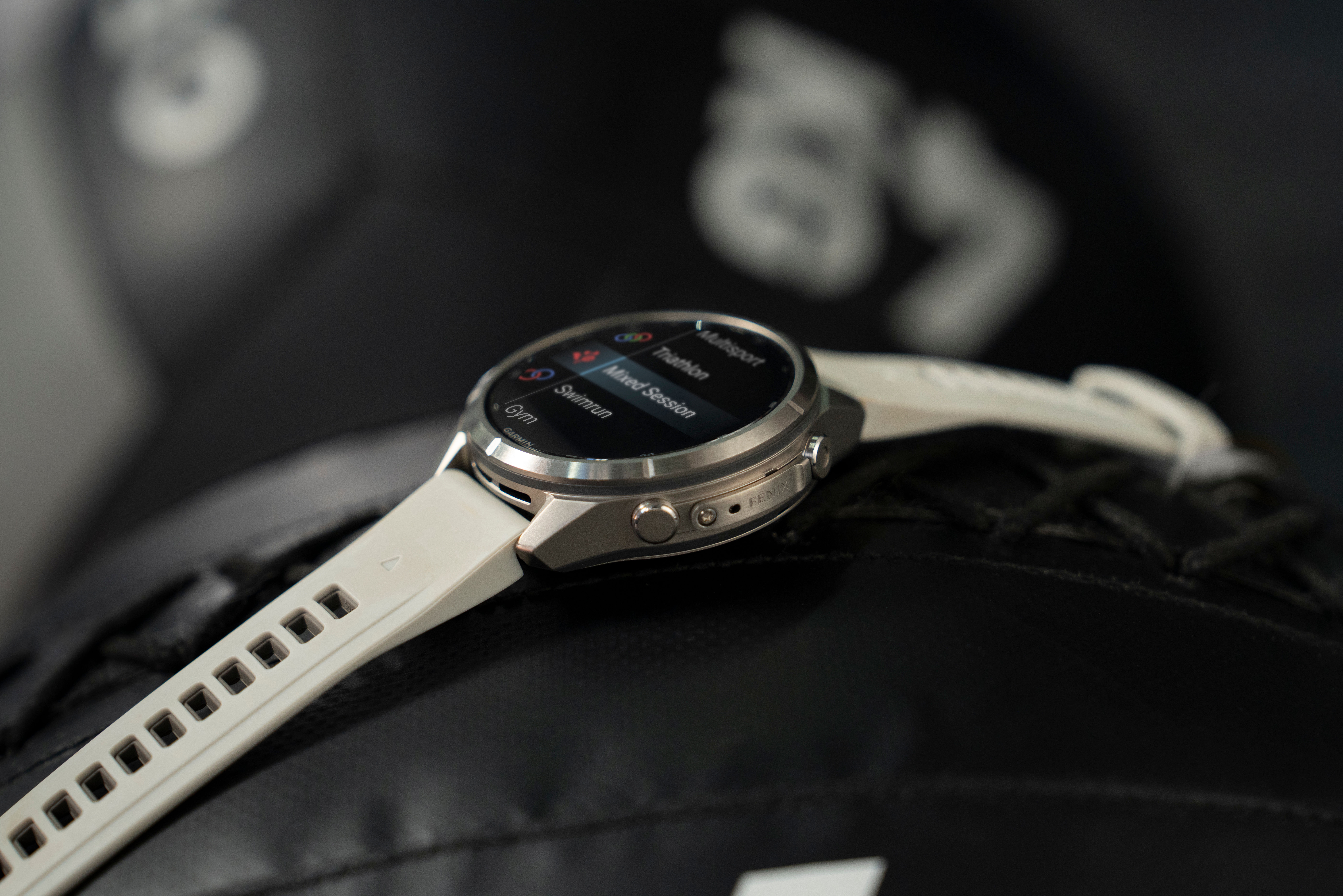 Eine silberne Smartwatch mit weißem Silikonarmband liegt auf einer dunklen, strukturierten Oberfläche.