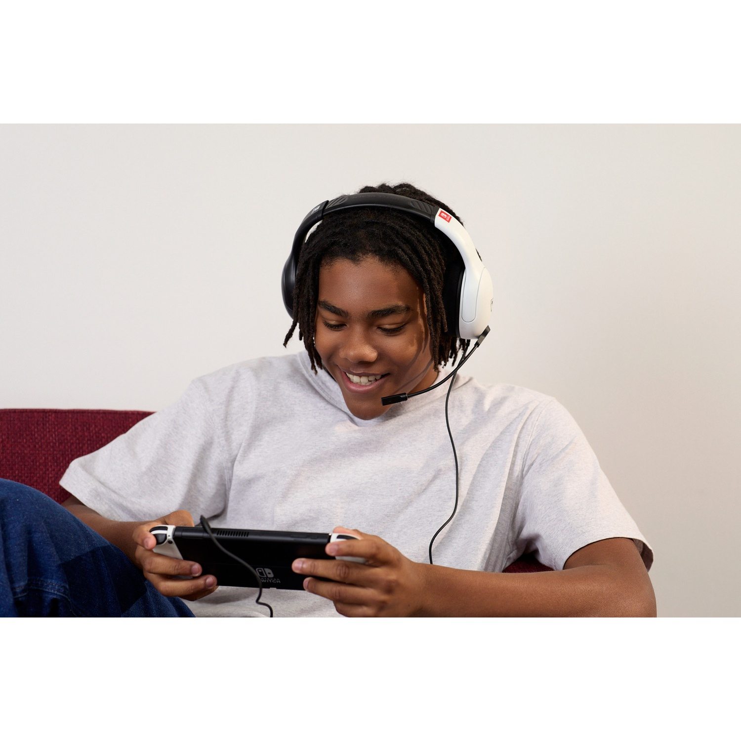 A smiling young person wearing headphones playing a handheld console on a couch.