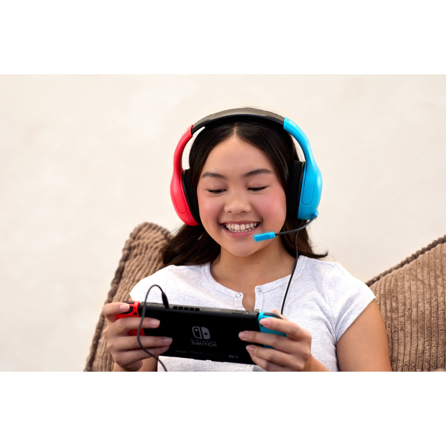 Smiling young woman wearing colorful headset and playing Nintendo Switch on a couch.
