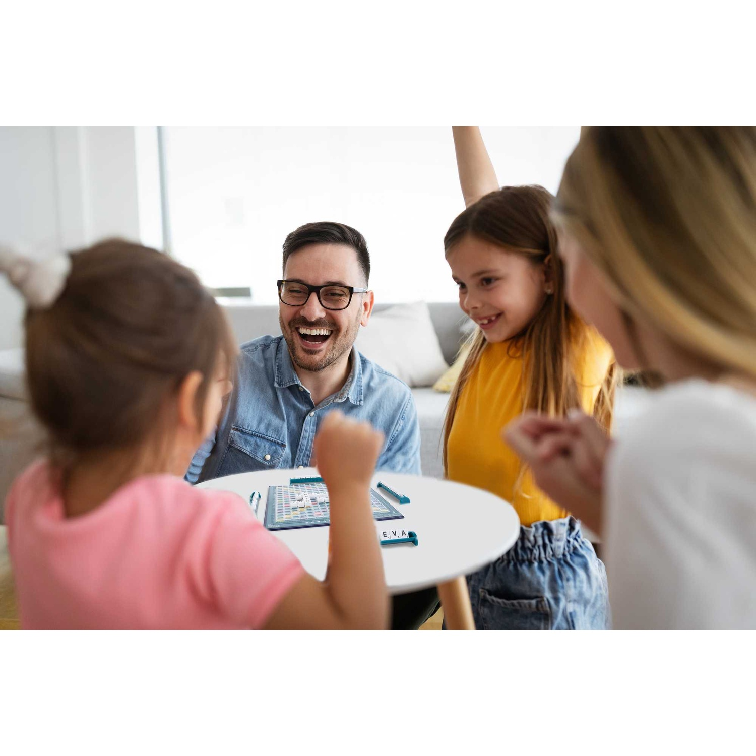 A happy family is laughing while playing a board game together around a small round table.