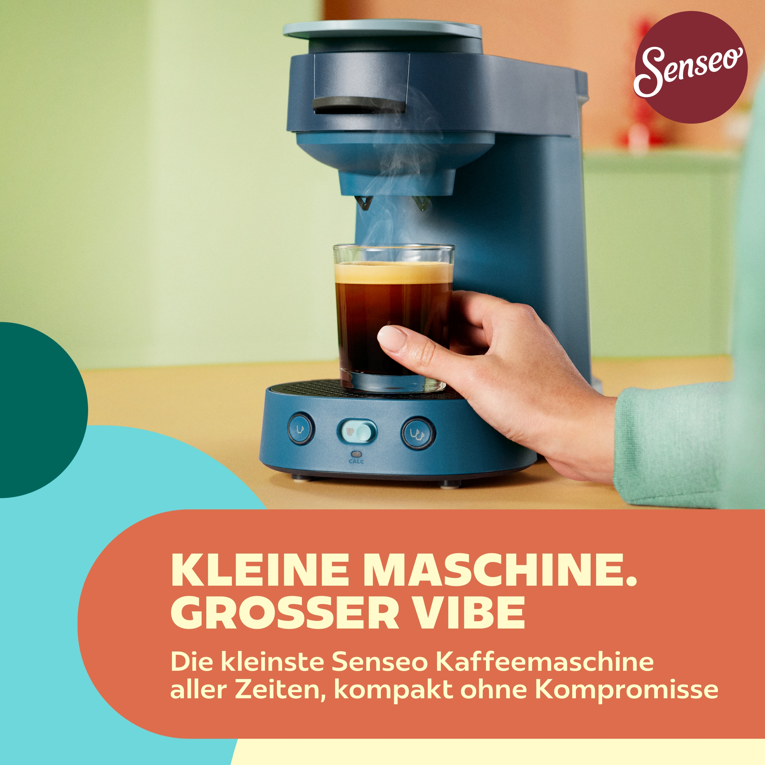 Eine blaue Senseo-Kaffeemaschine brüht Kaffee in ein Glas, gehalten von einer Hand auf einem Tisch.