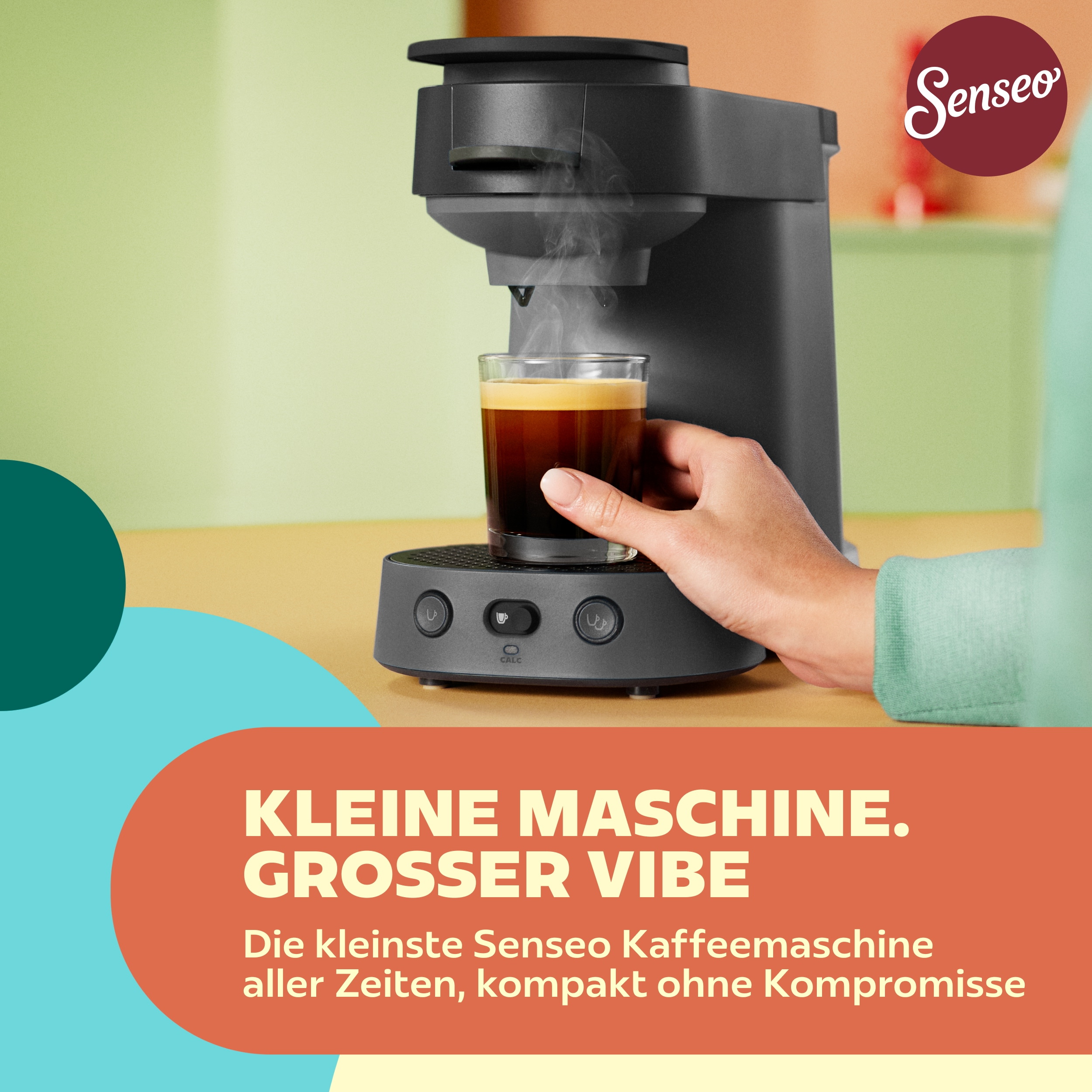 Eine schwarze Senseo-Kaffeemaschine brüht Kaffee in ein Glas, gehalten von einer Hand. Im Vordergrund Text.