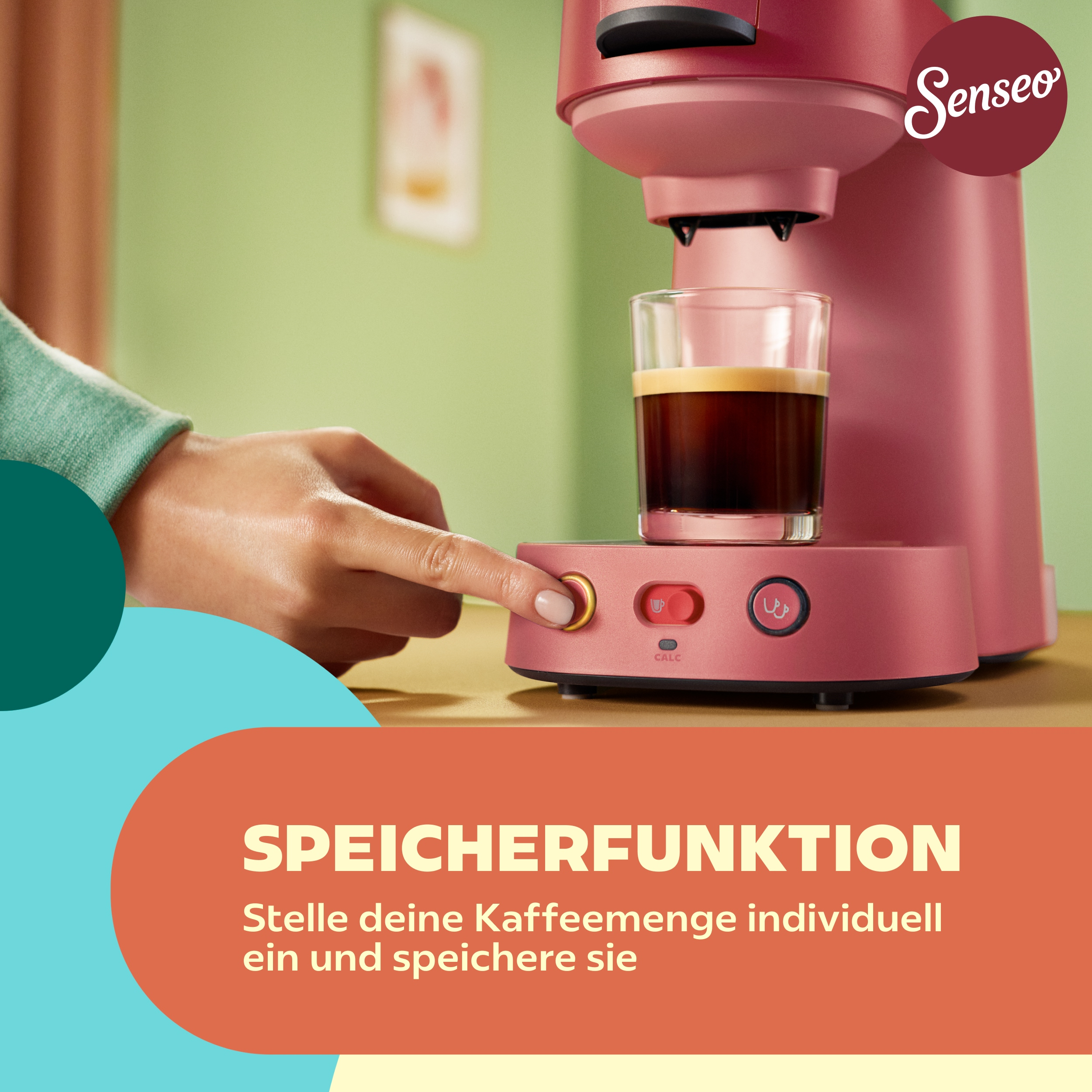 Eine Hand drückt den Startknopf einer rosa Senseo-Kaffeemaschine mit frisch gebrühtem Kaffee.