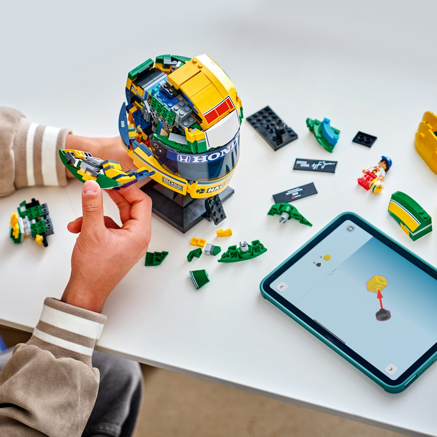 Una persona costruisce un casco Lego di Formula 1 giallo e verde, con istruzioni su un tablet.