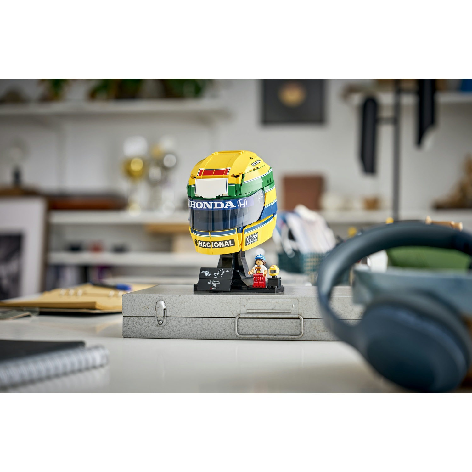Un casco F1 Lego giallo e verde su una scatola di metallo, con una minifigura e delle cuffie.