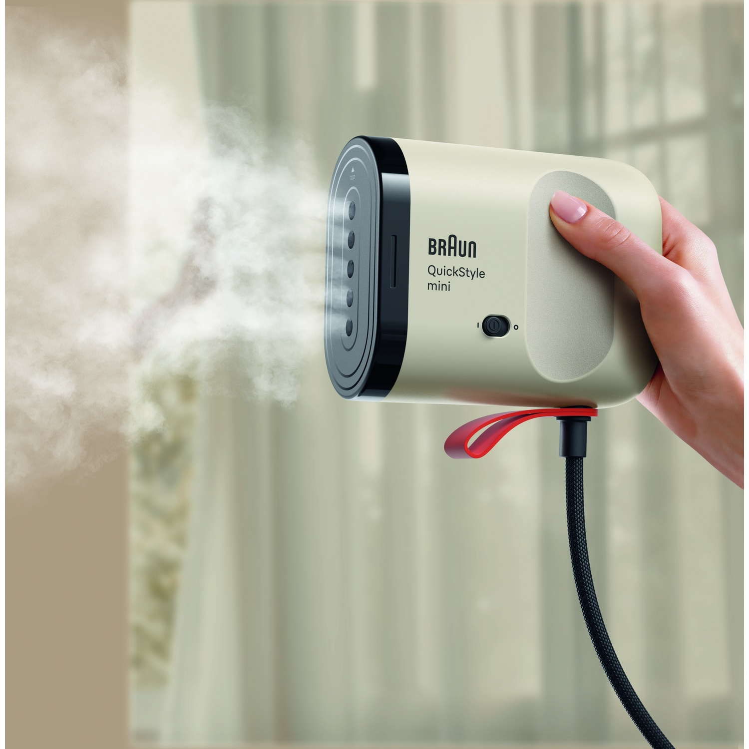 A hand holds the compact Braun QuickStyle mini garment steamer emitting steam.