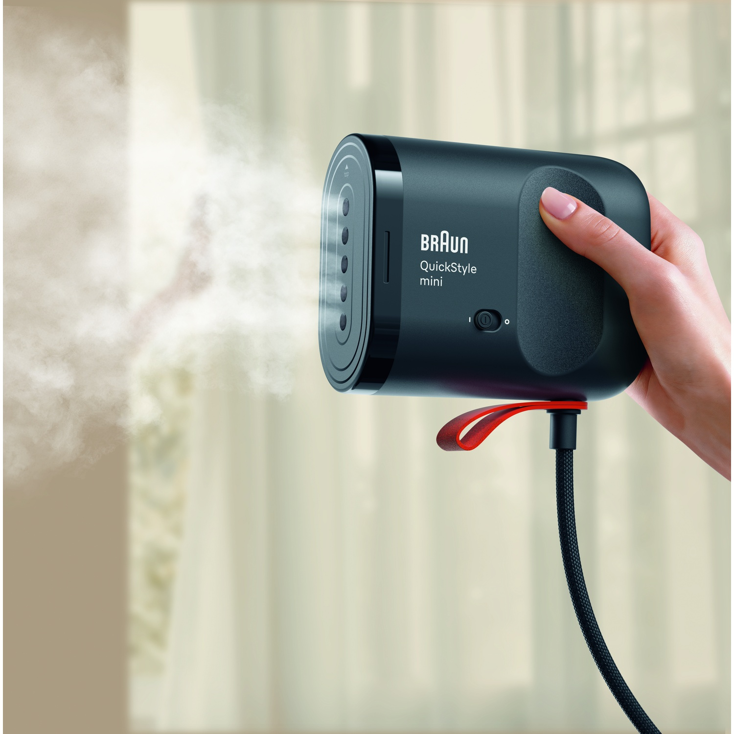 Een hand houdt een zwarte Braun QuickStyle mini kledingstomer vast die stoom uitblaast voor een lichte achtergrond.