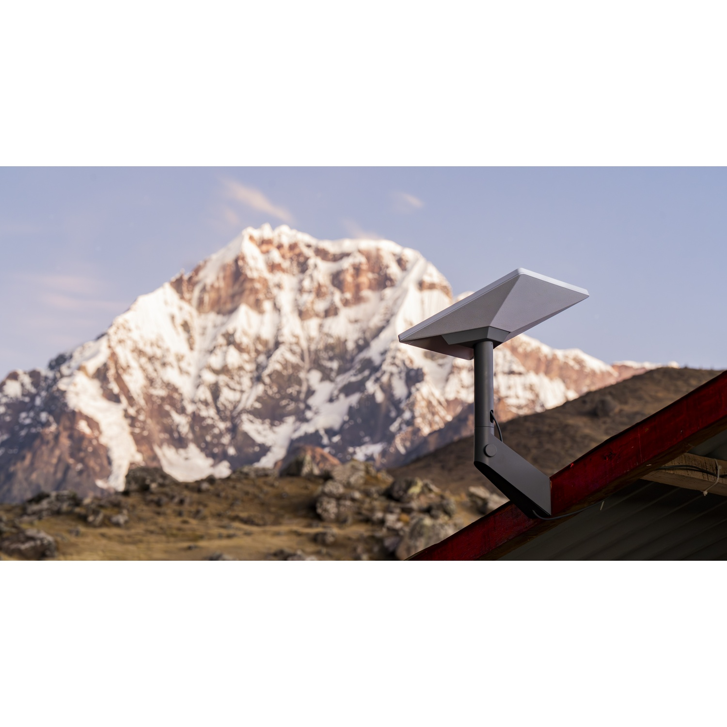 Una parabola satellitare è montata su un tetto rosso con montagne innevate sullo sfondo.