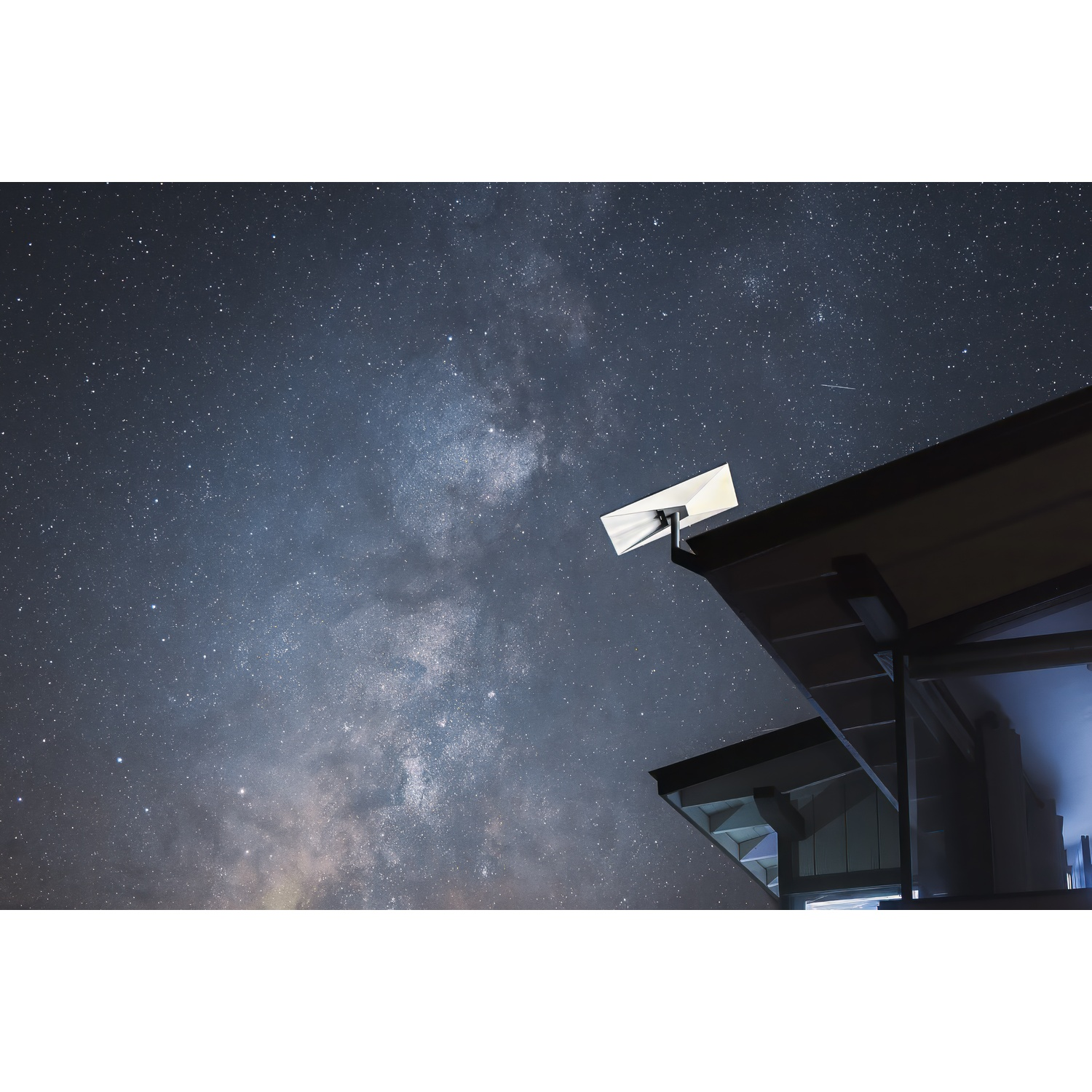 Una parabola satellitare sul tetto di una casa sotto un cielo notturno limpido con la Via Lattea visibile.