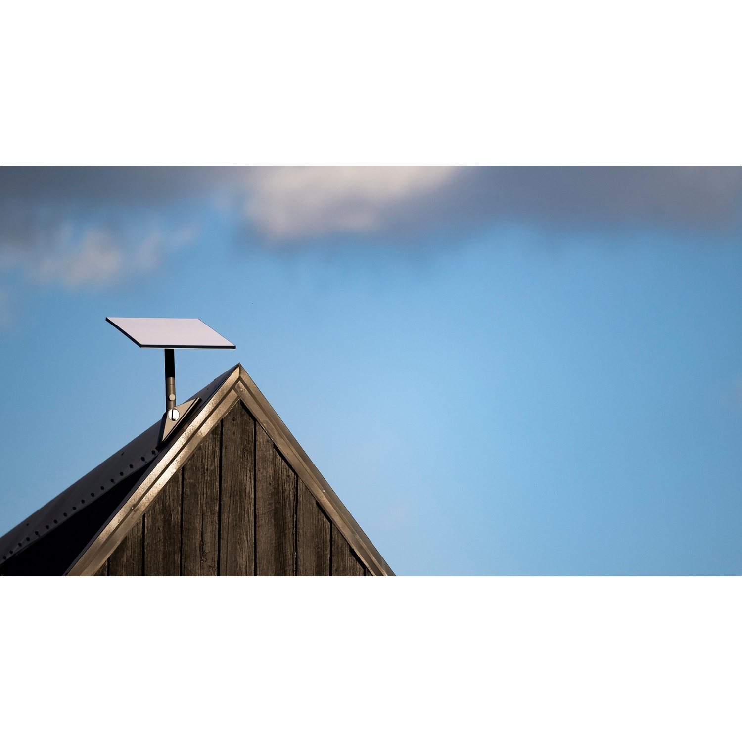 Una parabola satellitare sul tetto in legno di una casa contro un cielo azzurro con nuvole.