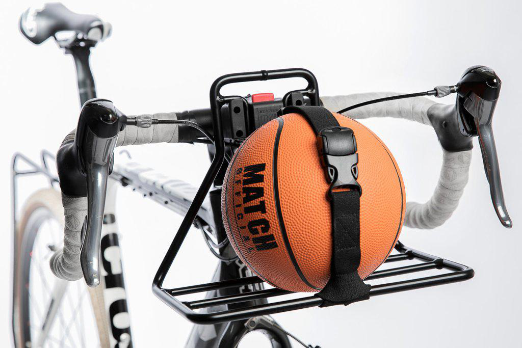 Ein orangefarbener Basketball wird mit einem Gurt auf dem vorderen Gepäckträger eines Rennrads transportiert.