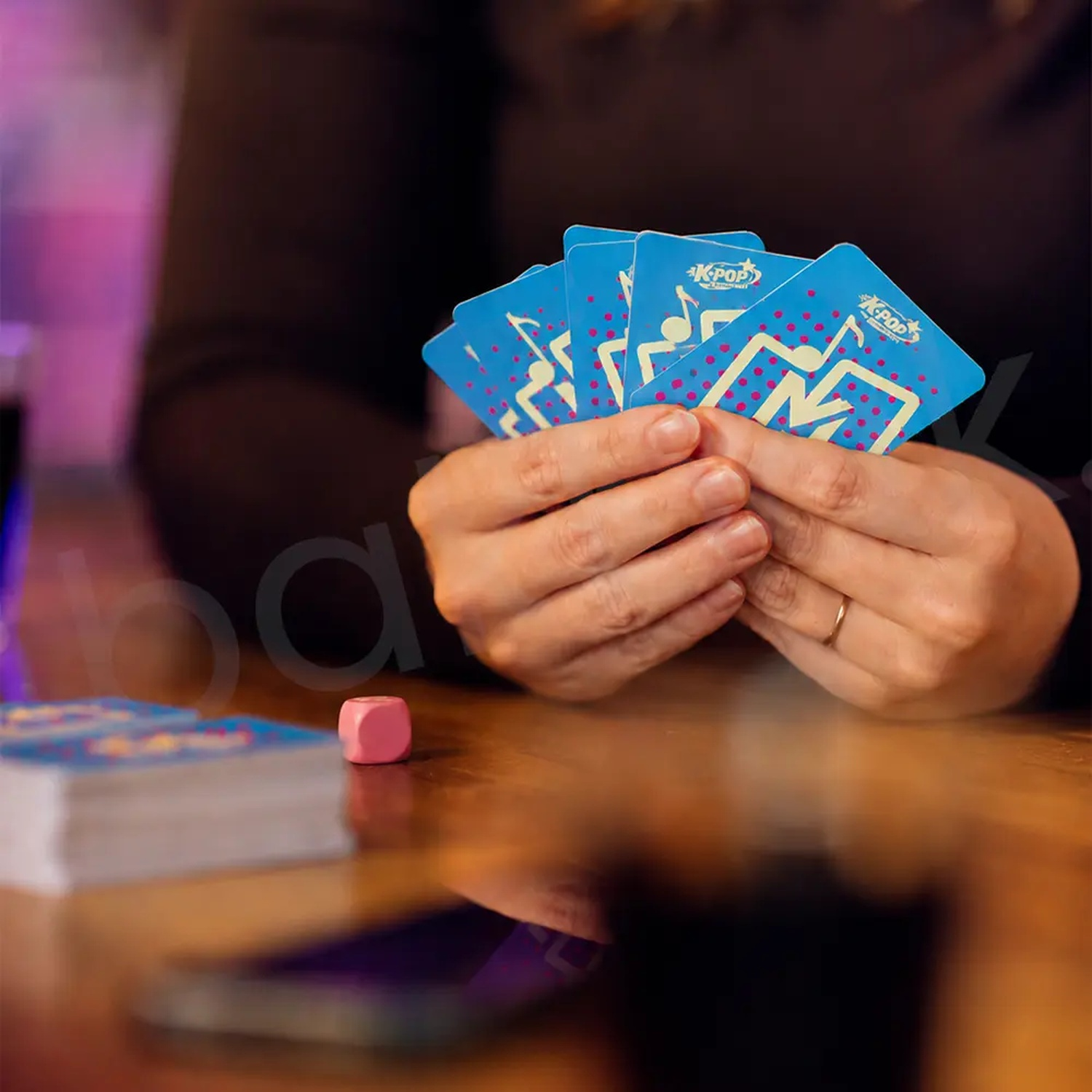 Person holds five blue K-Pop playing cards in hands at wooden table.