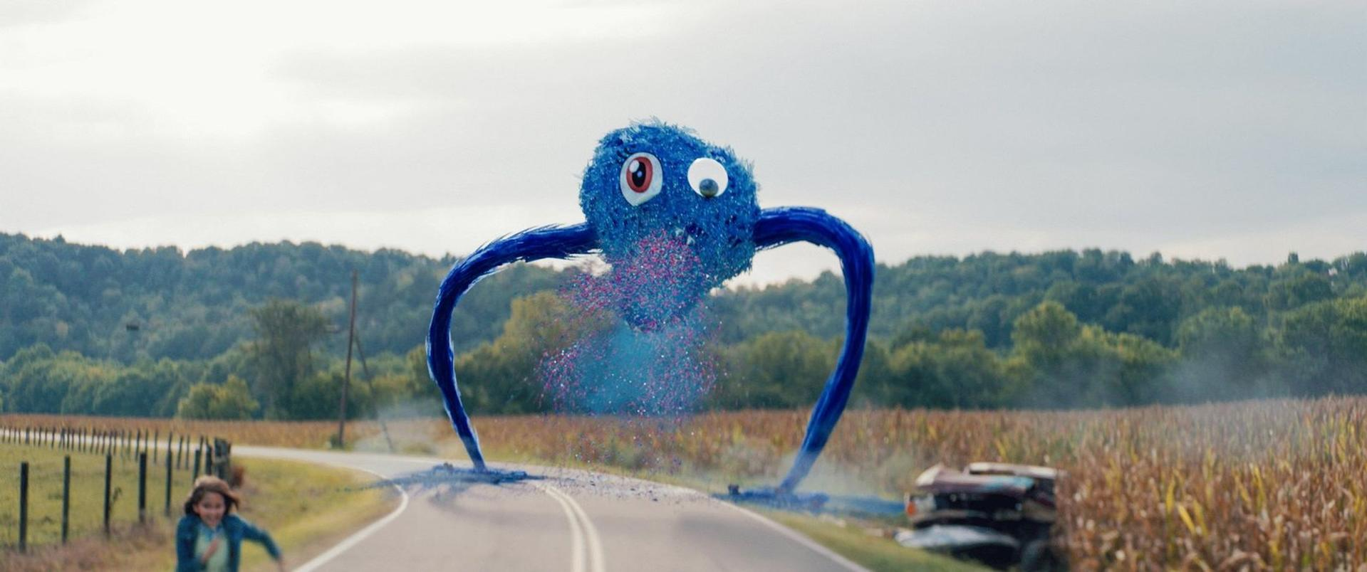 Ein großes, blaues, pelziges Monster mit riesigen googly Augen bricht auf einer ländlichen Straße in Konfetti aus.